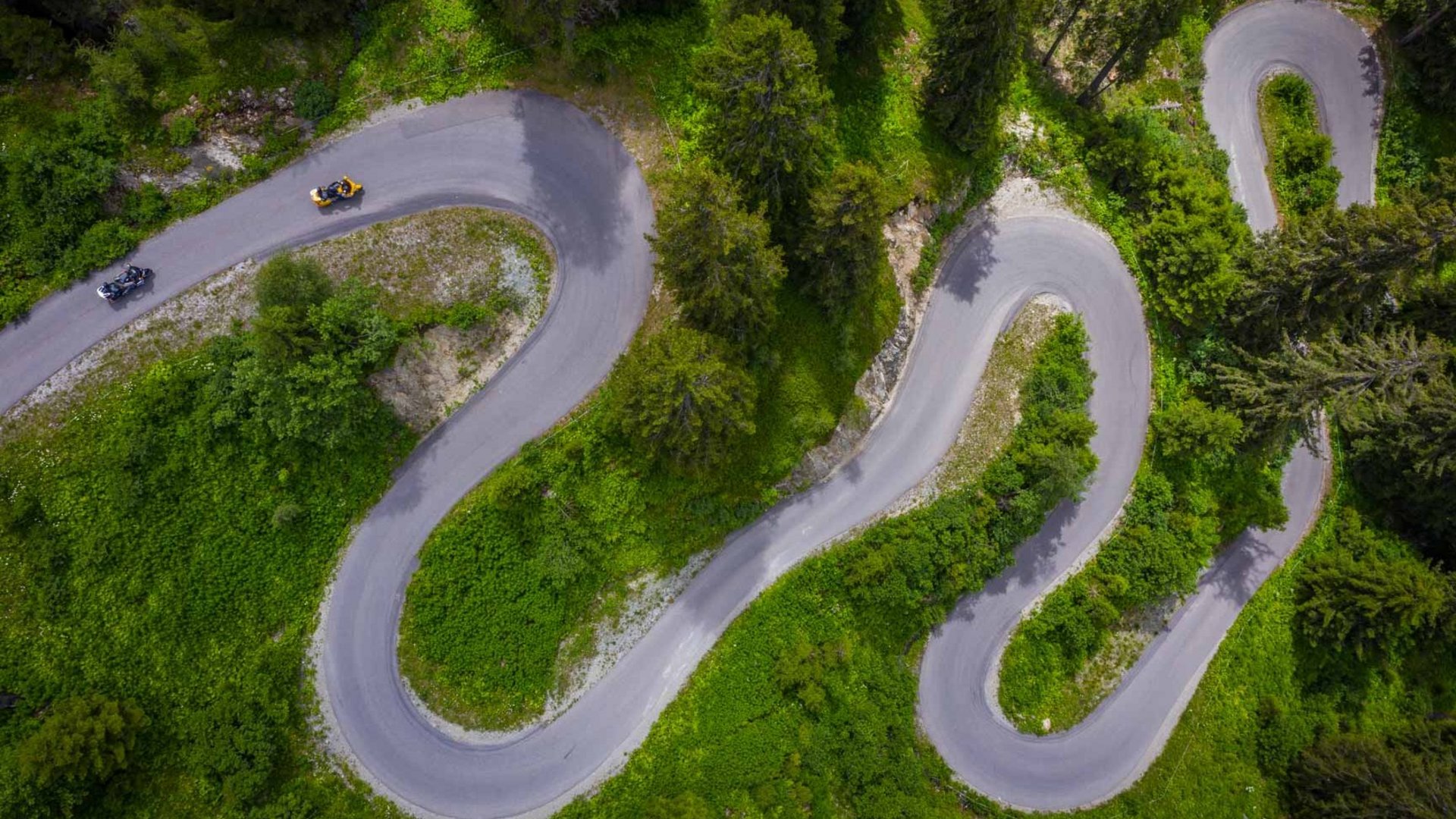 Luftaufnahme einer kurvigen Bergstraße mit zwei Motorrädern und grüner Vegetation (© Moppetfoto.de)